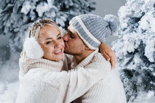 Couple seat on the snow and hug, kiss, and have fun each other. Winter love story before new year celebration. Waiting for christmas gift. Happy couple weared fur headphones, hats, white sweaters.