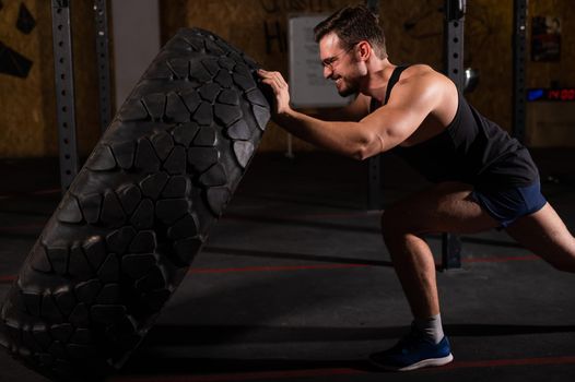 Caucasian man pushing a car tire in the gym