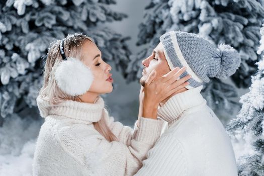 Couple seat on the snow and hug, kiss, and have fun each other. Winter love story before new year celebration. Waiting for christmas gift. Happy couple weared fur headphones, hats, white sweaters.