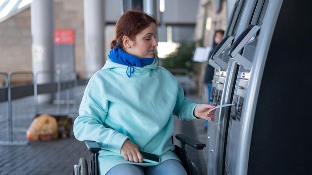 Caucasian woman in a wheelchair buys a ticket at a self-service ticket office