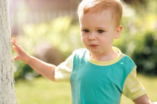 Portrait of a blond boy wearing a green t-shirt in the garden during the summertime.