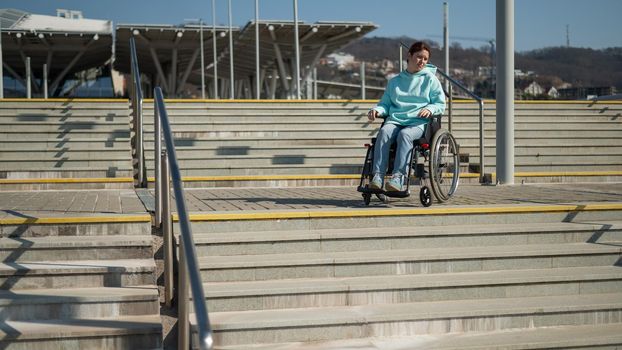 A caucasian woman in a wheelchair cannot go down stairs without a ramp. Hard to access environment