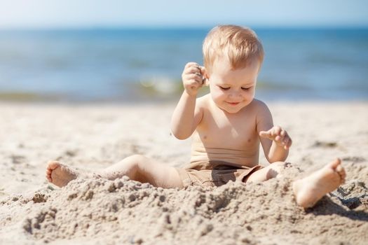 Beautiful little boy without shirt. Child playing in a summer beach on a sand. No sun protection for young child. A happy child is a little mischievous with sand.