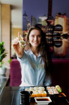 Happy girl is giving sushi to you in japanese restaurant. Young girl is holding sushi by chopsticks one piece of roll. Advert for sushi delivery.