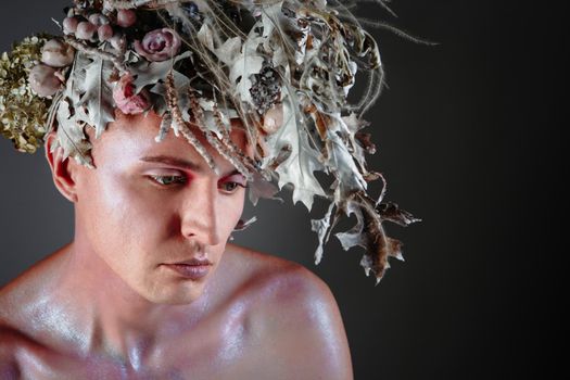 The face of a male model in a headdress of fresh flowers filled with wax