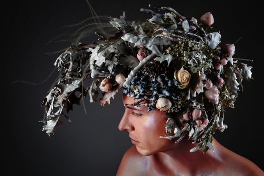 The face of a male model in a headdress of fresh flowers filled with wax