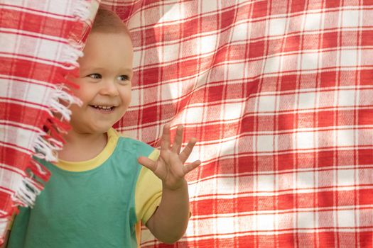 Happy little boy playing in the red checkered  shawl background