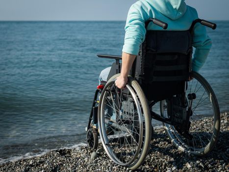 Caucasian woman in a wheelchair on the seashore. Close-up of female hands