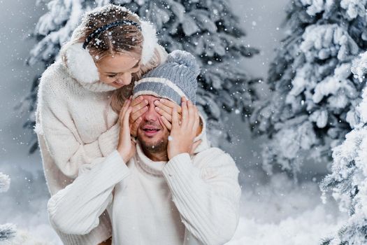 Couple seat on the snow and hug, kiss, and have fun each other. Winter love story before new year celebration. Waiting for christmas gift. Happy couple weared fur headphones, hats, white sweaters.