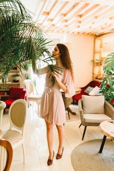 Tall dreamily girl takes palm tree into her hands and looks to the green leaves. Natural beauty. Stay at home