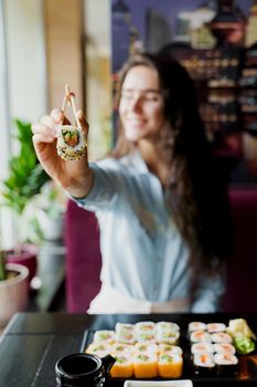 Happy girl is giving sushi to you in japanese restaurant. Young girl is holding sushi by chopsticks one piece of roll. Advert for sushi delivery.