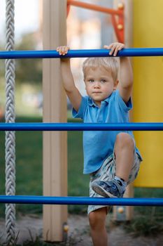 Small boy is climbing on a blue playground ladder. Looking at camera. Active child. Modern playground