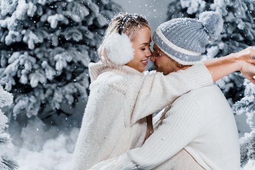 Couple seat on the snow and hug, kiss, and have fun each other. Winter love story before new year celebration. Waiting for christmas gift. Happy couple weared fur headphones, hats, white sweaters.