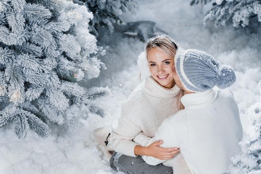 Man kiss and hug his woman and snow falls. New year love story. People weared wearing fur headphones, hats, white sweaters.