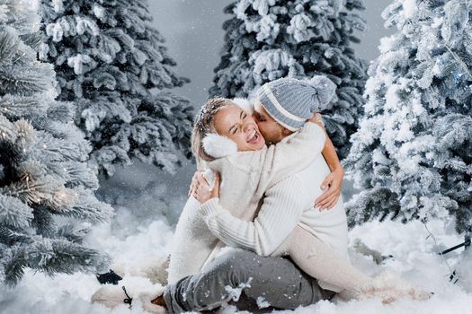 Couple seat on the snow and hug, kiss, and have fun each other. Winter love story before new year celebration. Waiting for christmas gift. Happy couple weared fur headphones, hats, white sweaters.