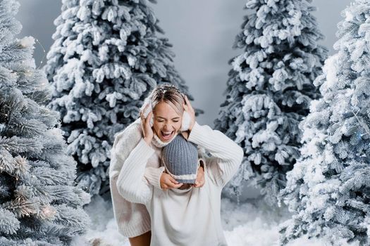 Falling snow and kisses. Happy young couple close-up hugs and kiss near christmas trees at the eve of new year celebration in winter day. Smiley man and woman weared white pullovers love each other