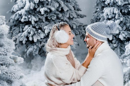 Couple seat on the snow and hug, kiss, and have fun each other. Winter love story before new year celebration. Waiting for christmas gift. Happy couple weared fur headphones, hats, white sweaters.