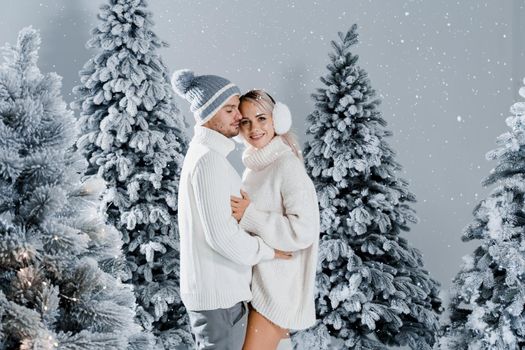 Couple hugging near christmass trees. Winter holidays. Love story of young couple weared white pullovers. Happy man and young woman love each other.