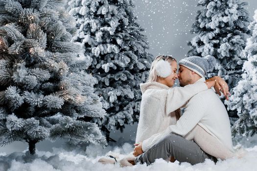 Couple hugging near christmass trees. Winter holidays. Love story of young couple weared white pullovers. Happy man and young woman love each other.