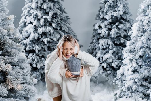 Couple couple laughing and having fun while snow falls near christmass trees. Winter holidays. Love story of young couple weared white pullovers. Happy man and young woman hug each other.