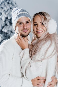 Couple hugging near christmass trees. Winter holidays. Love story of young couple weared white pullovers. Happy man and young woman love each other.