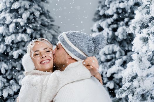 Winter love story at the eve of new year celebration. Couple hugging near christmass trees. Winter holidays. Love story of young couple weared white pullovers. Happy man and woman love each other.
