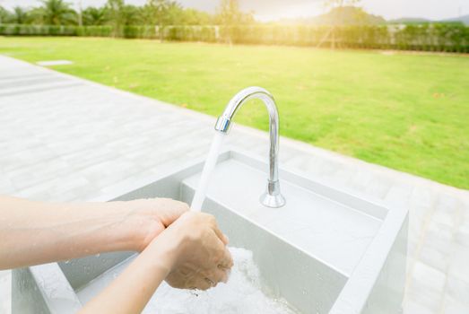 Woman washing hands with tap water under faucet at white sink. Washing hands with tap water at outdoor sink near grass field. Personal hygiene to prevent coronavirus or covid 19. Healthy lifestyle.