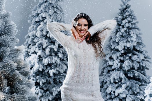 New year celebration.Happy girl with falling snow. Young woman weared in a warm white pullover and white socks. Winter holidays in snowy day