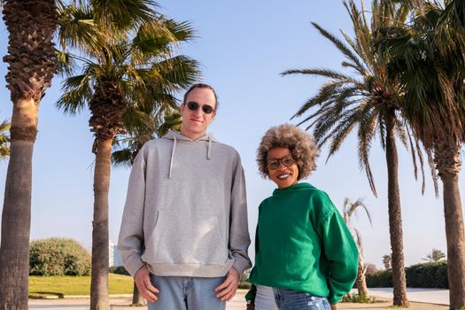 young caucasian man and latin woman smiling happy looking at camera next to palm trees, concept of friendship and couple relationship