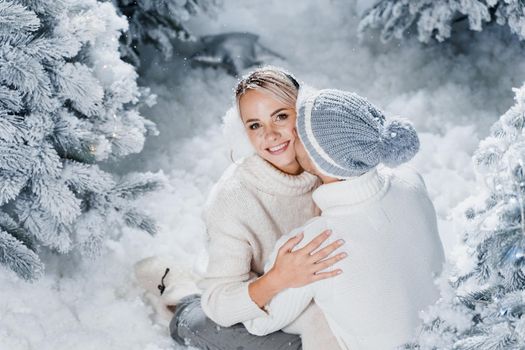 Handsome man is kissing his lovely girl in cheek. Winter holidays. Love story of young couple weared white pullovers. Happy man and young woman hug each other.