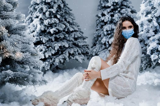 New year celebration at covid-19 coronavirus quarantine period. Happy girl in medical mask with falling snow stays at home. Social distance. Winter holidays in snowy day