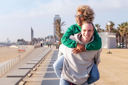 happy young couple smiling and having fun with the woman piggybacked by her boyfriend, concept of friendship and fun in a relationship, copy space for text