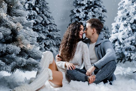 New year love story. Couple kiss and hug, snow is falling. Happy young couple near christmas trees in winter day.