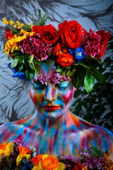 Portrait of a girl whose face is painted with colored paints in a wreath of flowers.