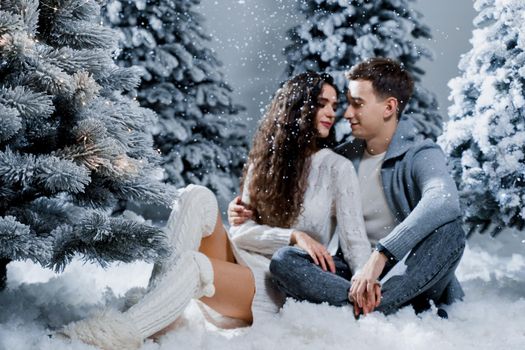 Falling snow on the blurred couple background. New year love story. Couple kiss and hug. Happy young couple near christmas trees in winter day.