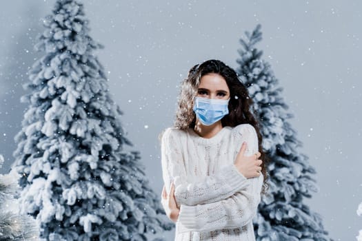 New year celebration at covid-19 coronavirus quarantine period. Happy girl in medical mask with falling snow stays at home. Social distance. Winter holidays in snowy day