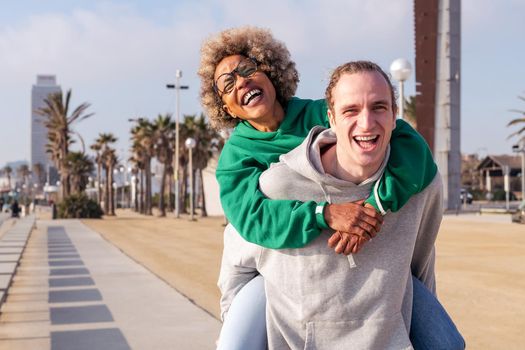 happy young couple laughing and having fun with the man piggybacking her girlfriend, concept of friendship and fun in a relationship, copy space for text