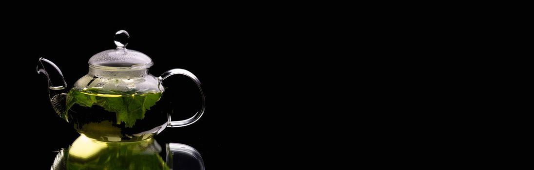 Hot glass teapot on a black background, green mint tea. Herbal tea and healthy drink concept