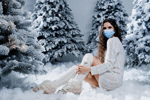 New year celebration at covid-19 coronavirus quarantine period. Happy girl in medical mask with falling snow stays at home. Social distance. Winter holidays in snowy day