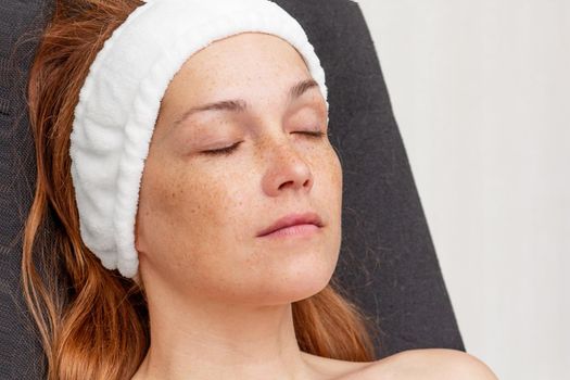 Caucasian middle-aged woman with white band on head without make-up relaxing in chair with closed eyes
