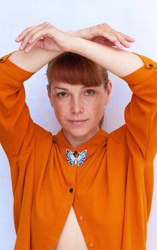 Caucasian middle-aged woman in orange holding arms like butterfly over light blue background