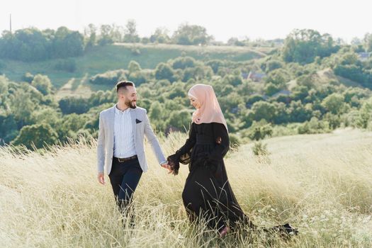 Muslim love story of mixed couple. Man and woman smiles and walks on the green hills . Woman weared in hijab looks to her man. Advert for on-line dating agency