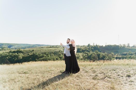 Muslim love story of mixed couple. Man and woman smiles and walks on the green hills . Woman weared in hijab looks to her man. Advert for on-line dating agency