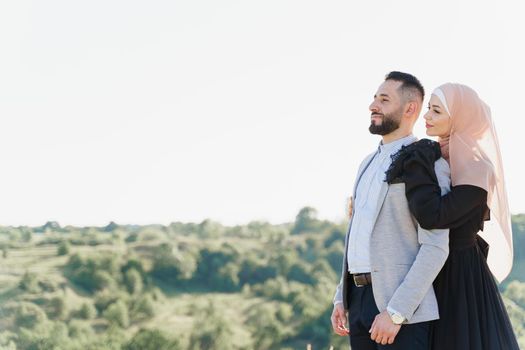 Muslim love story. Mixed couple smiles and hugs on the green hills . Woman weared in hijab looks to her man. Advert for on-line dating agency