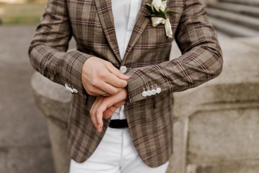 Groom in brown plaid jacket looks at his ring on the finger. Advert for wedding agency