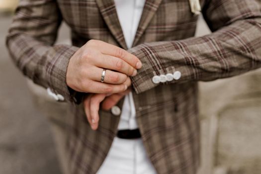 Groom in brown plaid jacket looks at his ring on the finger. Advert for wedding agency