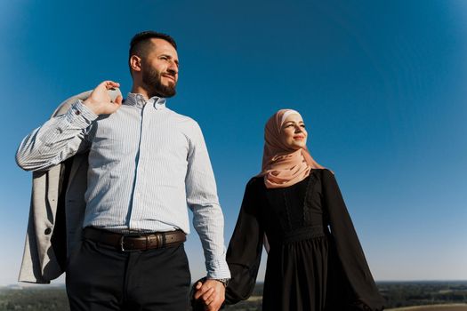 Muslim love story on the blue sky background. cheerful mixed couple smiles and hugs . Woman weared in hijab looks to her man. Advert for on-line dating agency