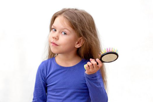 Isolated caucasian little girl of 5-6 years with long hair and hair brush with hair on it, looking at camera on white background in blue
