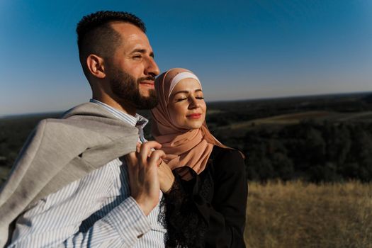 Muslim love story on the blue sky background. cheerful mixed couple smiles and hugs . Woman weared in hijab looks to her man. Advert for on-line dating agency