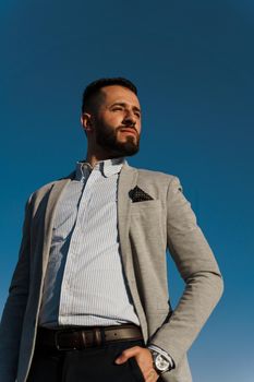 Handsome bearded arabian man in sunglasses on the blue sky background. Confident muslim business man. Arab man weared in grey coat